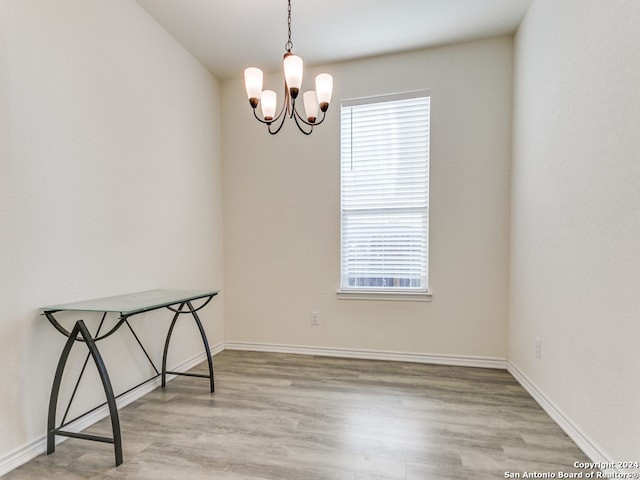 spare room featuring a chandelier, a healthy amount of sunlight, and light wood-type flooring