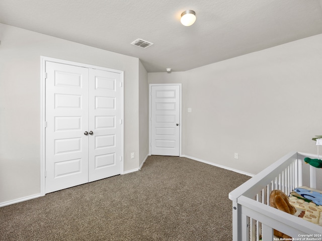 unfurnished bedroom with dark colored carpet, a closet, a textured ceiling, and a nursery area