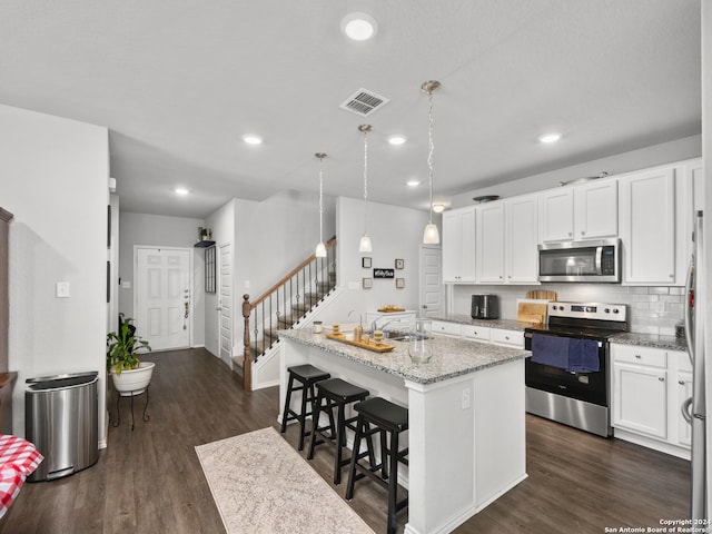 kitchen featuring light stone countertops, hanging light fixtures, an island with sink, white cabinets, and appliances with stainless steel finishes