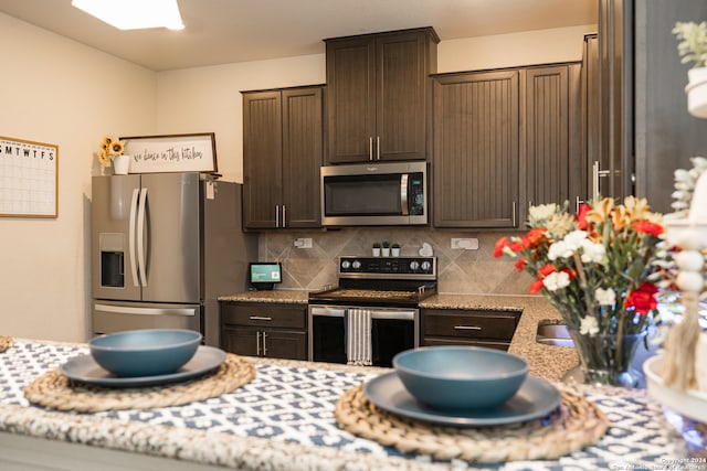 kitchen with dark brown cabinets, light stone counters, appliances with stainless steel finishes, and tasteful backsplash