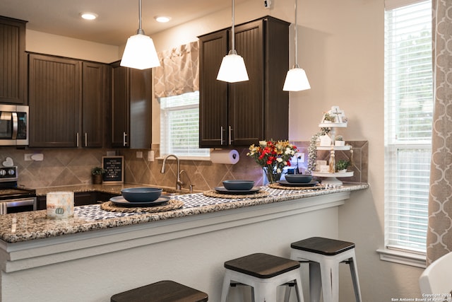 kitchen featuring decorative backsplash, light stone counters, stainless steel appliances, and decorative light fixtures