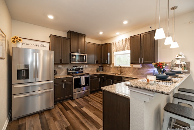 kitchen featuring light stone countertops, hanging light fixtures, dark hardwood / wood-style floors, a kitchen bar, and appliances with stainless steel finishes