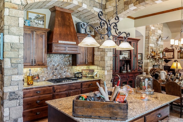 kitchen with light stone countertops, premium range hood, stainless steel gas cooktop, and hanging light fixtures