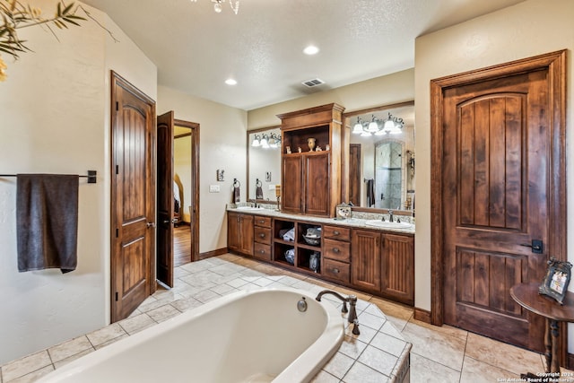 bathroom featuring tile patterned flooring, vanity, a textured ceiling, and tiled bath