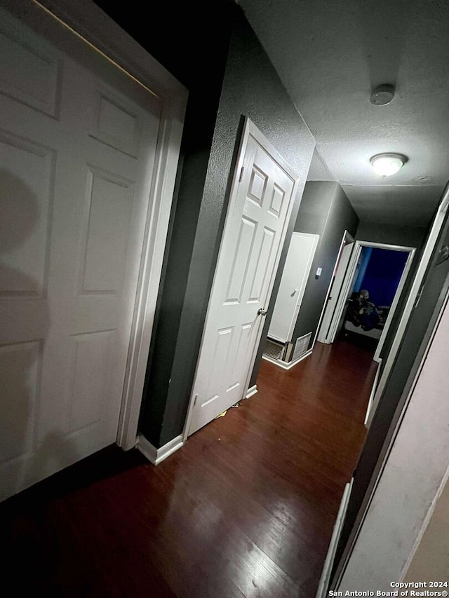 hallway with a textured ceiling and dark hardwood / wood-style flooring