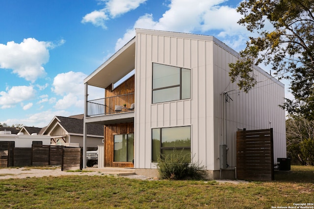 rear view of property featuring a lawn, cooling unit, and a balcony