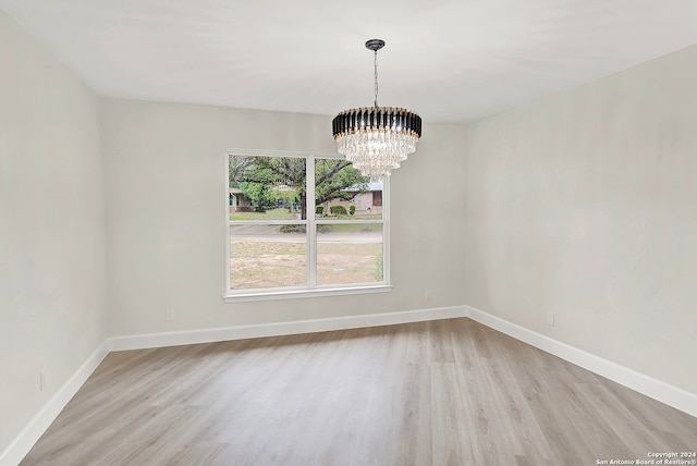 empty room with light wood-type flooring and a notable chandelier