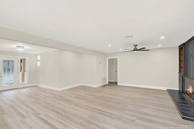 unfurnished living room with ceiling fan, a tile fireplace, and light hardwood / wood-style flooring