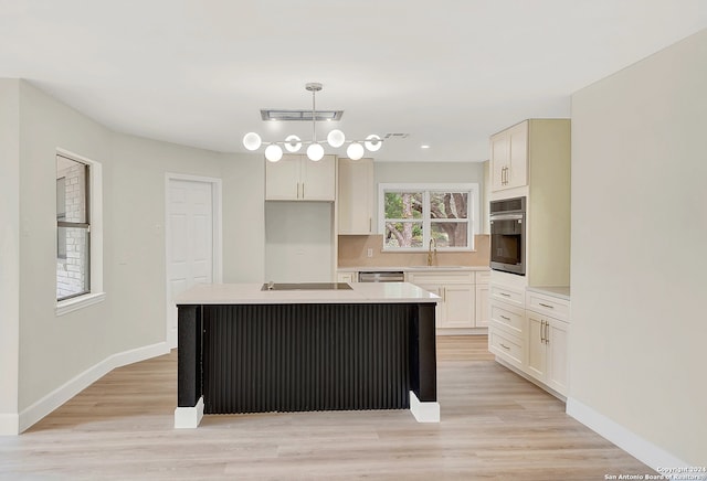 kitchen with appliances with stainless steel finishes, sink, pendant lighting, light hardwood / wood-style floors, and a kitchen island