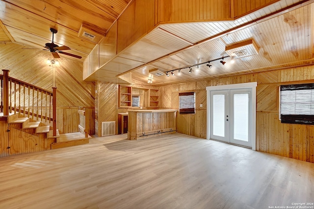 unfurnished living room with wood walls, lofted ceiling, french doors, ceiling fan, and light wood-type flooring