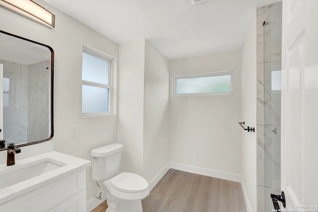 bathroom featuring hardwood / wood-style floors, vanity, a tile shower, and toilet