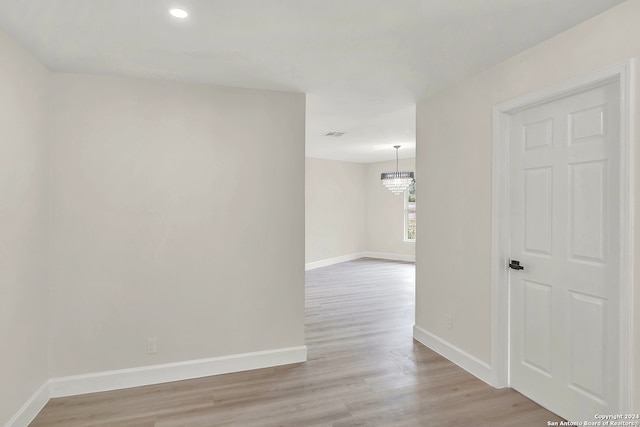 corridor with light wood-type flooring and an inviting chandelier