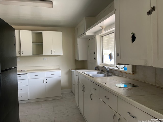 kitchen featuring decorative backsplash, white cabinetry, black refrigerator, and sink