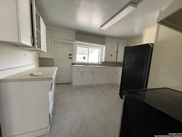 kitchen featuring white cabinets, black refrigerator, and sink