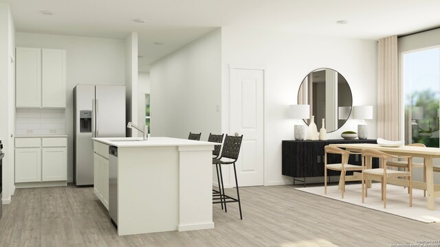 kitchen with white cabinets, decorative backsplash, light wood-type flooring, an island with sink, and appliances with stainless steel finishes