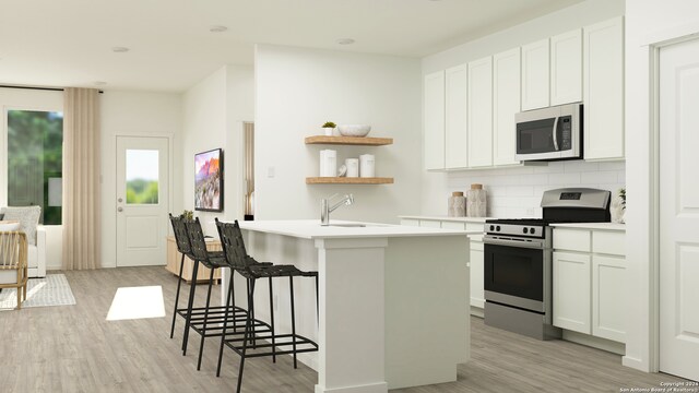 kitchen with white cabinets, a center island with sink, sink, appliances with stainless steel finishes, and light hardwood / wood-style floors