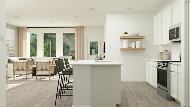 kitchen with a breakfast bar, a kitchen island with sink, white cabinets, sink, and appliances with stainless steel finishes