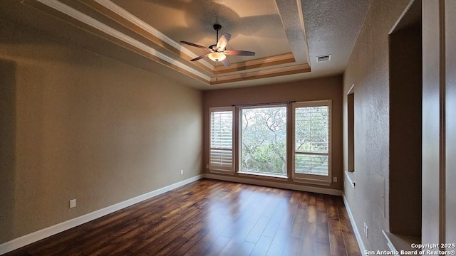 spare room featuring dark wood finished floors, a raised ceiling, visible vents, ornamental molding, and baseboards