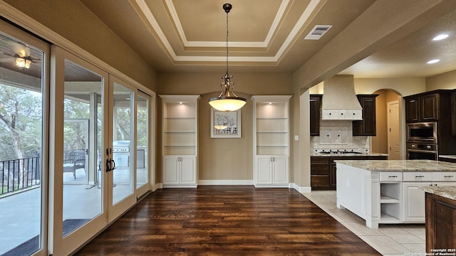 kitchen featuring visible vents, a raised ceiling, stainless steel appliances, wall chimney range hood, and open shelves