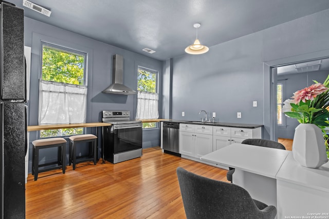 kitchen featuring plenty of natural light, wall chimney exhaust hood, light hardwood / wood-style floors, and appliances with stainless steel finishes