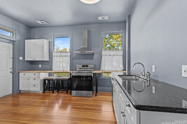 kitchen featuring white cabinetry, stainless steel electric range, wall chimney range hood, and light wood-type flooring