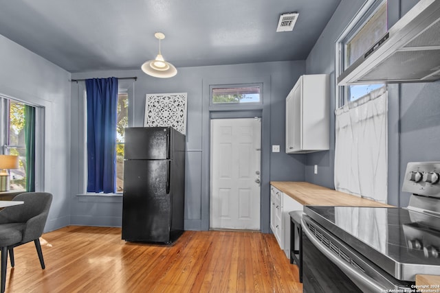 kitchen featuring black refrigerator, light wood-type flooring, stainless steel electric range oven, range hood, and white cabinetry