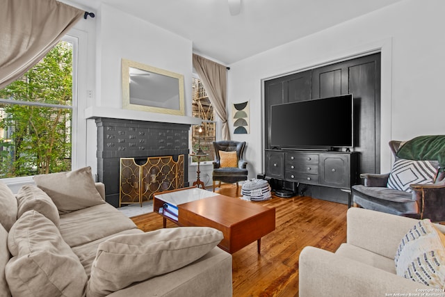 living room featuring hardwood / wood-style flooring, ceiling fan, and a brick fireplace