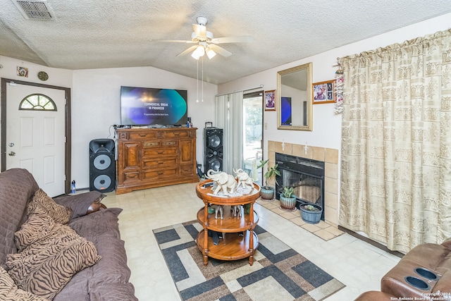 living room featuring ceiling fan, a textured ceiling, a tile fireplace, and vaulted ceiling