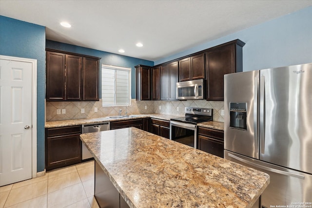 kitchen featuring stainless steel appliances, light tile patterned floors, light stone counters, dark brown cabinets, and a kitchen island