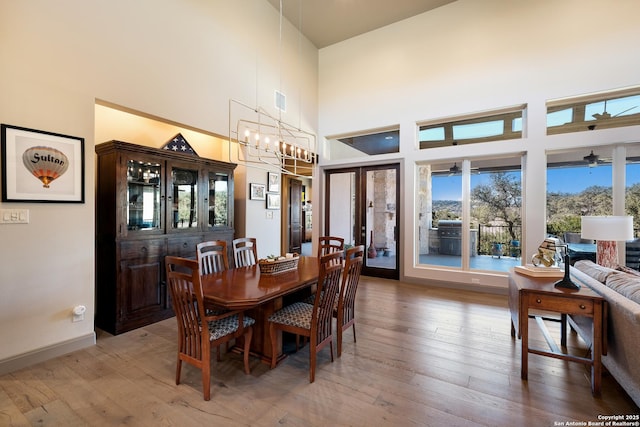 dining space with a towering ceiling, wood-type flooring, and a notable chandelier