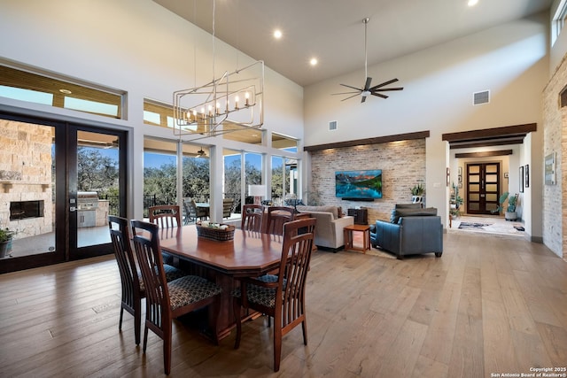 dining space featuring ceiling fan with notable chandelier, light hardwood / wood-style floors, and a high ceiling