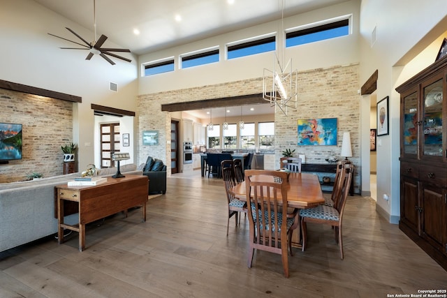 dining area featuring hardwood / wood-style floors, a towering ceiling, and ceiling fan with notable chandelier