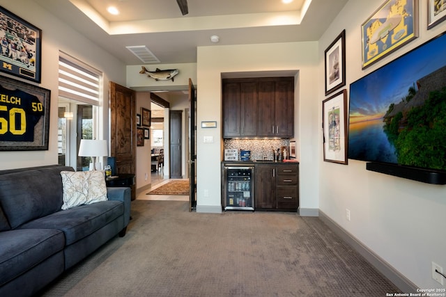 carpeted living room with wine cooler, bar, and a tray ceiling