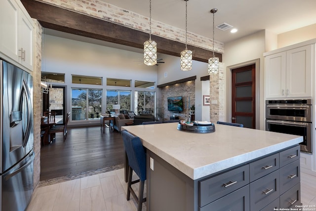 kitchen with white cabinets, beamed ceiling, pendant lighting, a kitchen island, and appliances with stainless steel finishes