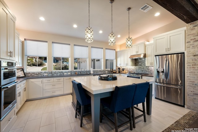 kitchen with tasteful backsplash, white cabinets, a breakfast bar area, a kitchen island, and appliances with stainless steel finishes