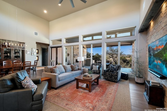 living room with a towering ceiling, ceiling fan with notable chandelier, and hardwood / wood-style flooring