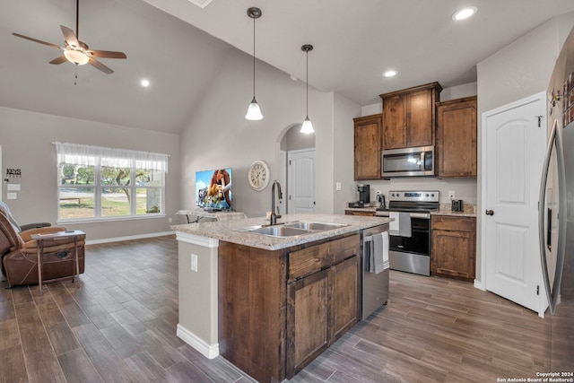 kitchen featuring sink, dark wood-type flooring, stainless steel appliances, high vaulted ceiling, and an island with sink