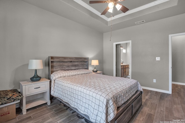 bedroom featuring dark hardwood / wood-style flooring, a tray ceiling, ceiling fan, and connected bathroom