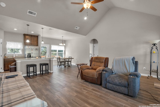 living room with ceiling fan with notable chandelier, high vaulted ceiling, and dark wood-type flooring