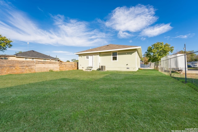 rear view of house with central AC and a lawn