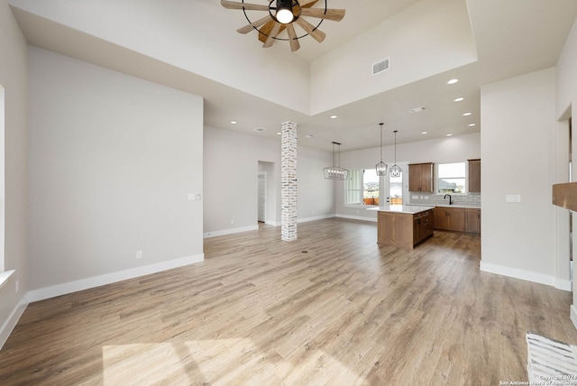 unfurnished living room featuring a high ceiling, sink, light hardwood / wood-style flooring, ceiling fan, and ornate columns