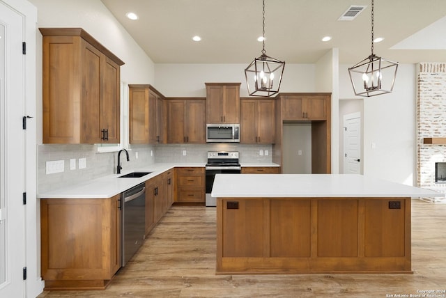 kitchen with appliances with stainless steel finishes, light wood-type flooring, a kitchen island, and sink