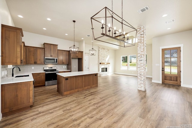 kitchen featuring pendant lighting, a center island, ornate columns, appliances with stainless steel finishes, and light hardwood / wood-style floors