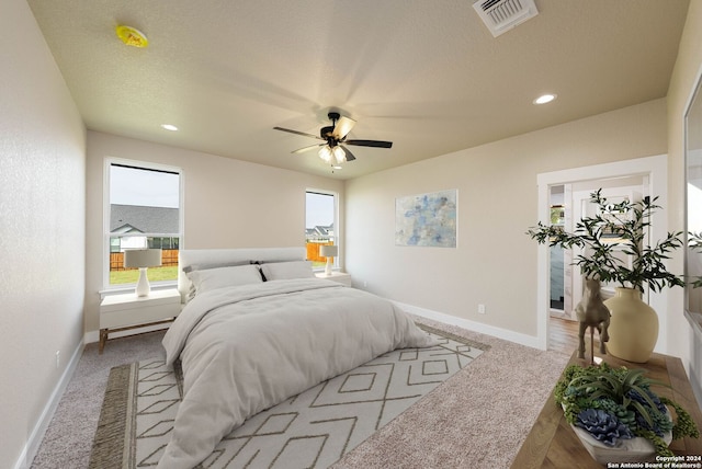 bedroom with ceiling fan, light colored carpet, and a textured ceiling