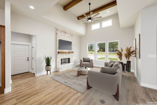 living room with ceiling fan, a high ceiling, light hardwood / wood-style flooring, beamed ceiling, and a fireplace