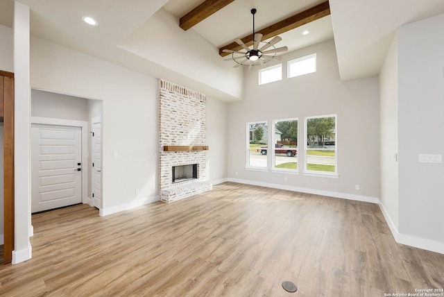 unfurnished living room with a towering ceiling, ceiling fan, beam ceiling, light hardwood / wood-style flooring, and a fireplace