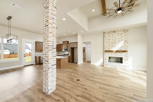 unfurnished living room featuring a high ceiling, ceiling fan with notable chandelier, light wood-type flooring, a fireplace, and decorative columns