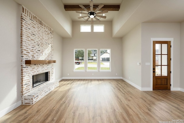 unfurnished living room featuring ceiling fan, a fireplace, beamed ceiling, and light wood-type flooring