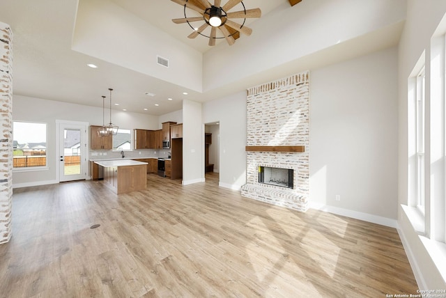 unfurnished living room featuring a high ceiling, light hardwood / wood-style flooring, ceiling fan, and a stone fireplace