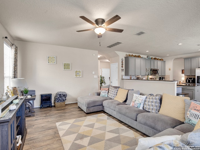 living room featuring ceiling fan, a textured ceiling, and light wood-type flooring